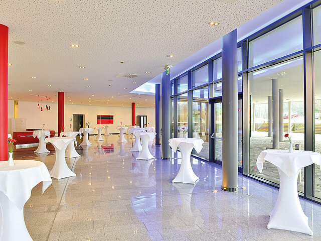 Das Foyer des Convention Centers mit weiß eingekleideten Stehtischen, roten und blau beleuchteten Säulen und einer Glasfront