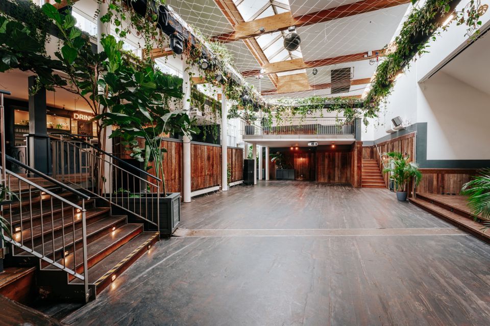 Das leere Atrium unter dem Glasdach — Galerien über drei Ebenen, Bar links, Podest rechts