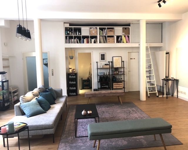 Der Loungebereich mit Sofa und Bänken, dahinter Getränkeregal und Aufgang zur Empore