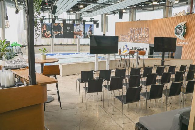 Stuhlreihen vor zwei Monitoren in der Halle, dahinter die Welle und der Jochen-Schweizer-Schriftzug auf einer Holzwand