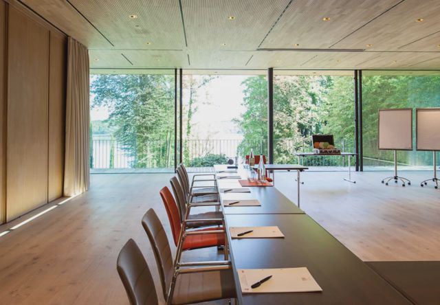 Der Gartenpavillon in U-Form, auf zwei Seiten bodentief verglast mit Blick durch die Bäume auf den See