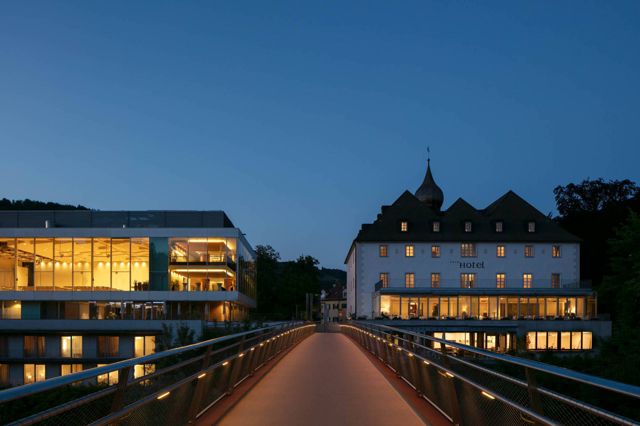 Schloss und Glasbau am Abend, beleuchtet, mit Brücke