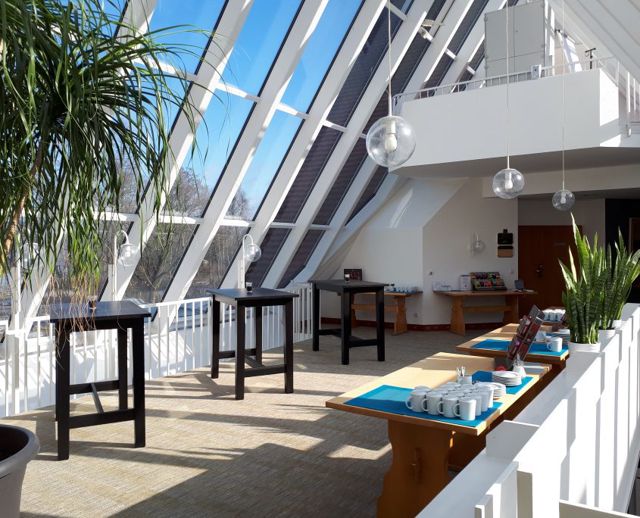 Die Tagungsgalerie unter einem schrägen Glasdach, mit Stehtischen und einer Kaffeestation zum See hin
