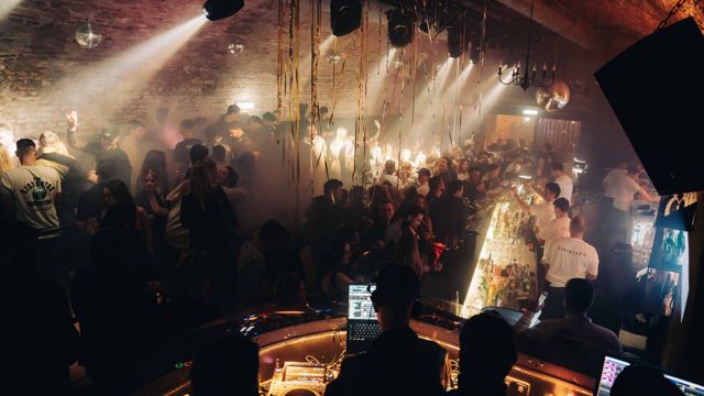 Volle Clubnacht im Eiskeller: Lichtkegel durch den Nebel, Gäste an der langen Bar, im Vordergrund das DJ-Pult