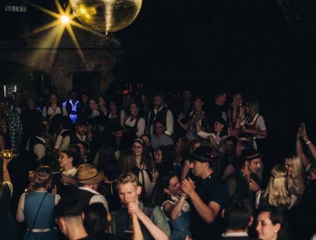 Trachtenparty im Gewölbe: Gäste in Dirndl und Lederhose unter Discokugel und Scheinwerfern