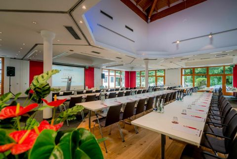 Der Seminar-Pavillon mit langen Tischreihen unter einem erhöhten Dachaufsatz aus Holz, roten Wandflächen und Fenstern ins Grüne