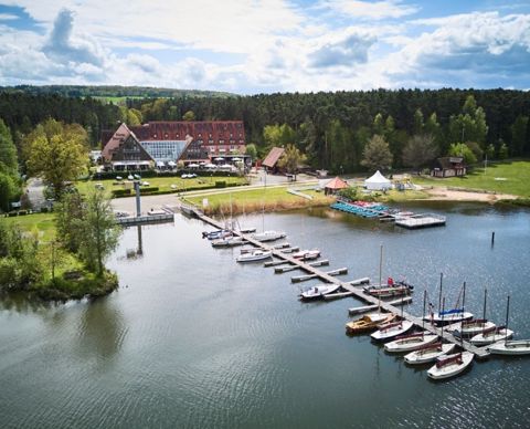 Das Hotel von oben: ein langgestreckter Bau mit rotem Dach am Waldrand, davor Liegewiese, Bootsstege und Segelboote auf dem Brombachsee